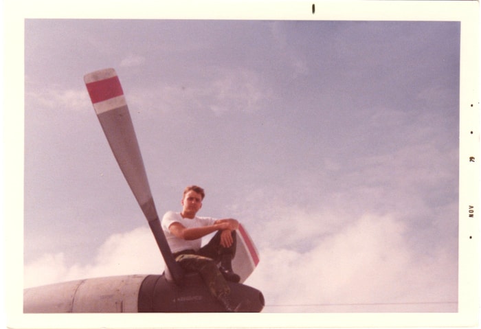 Crew member seated on aircraft wing propeller