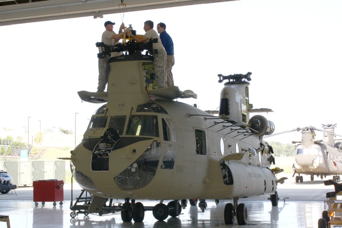 Technicians performing maintenance on a Chinook helicopter in a hangar