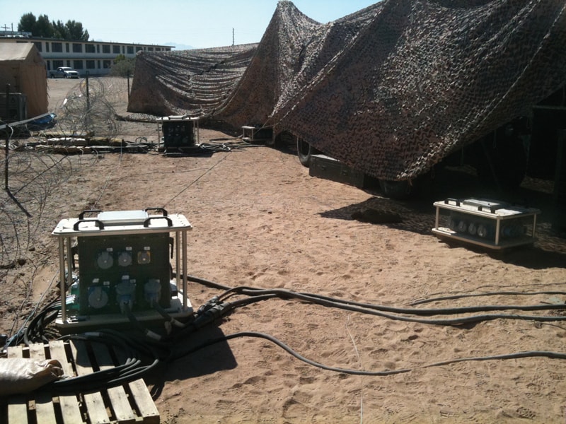 Military field power distribution units under camouflage netting